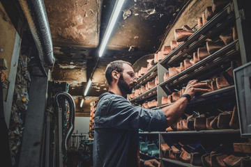 Focused bearded cobbler is looking for right shoe form at the storage.