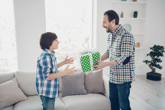 Profile side view portrait of two nice lovely cheerful cheery glad guys dad daddy giving festal box gift to pre-teen son in light white modern interior house living-room indoors