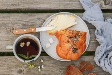 Scythe with poppy seeds, butter and tea. Baking with poppy seeds and coffee. The work of a baker. Poppy seed baking and pies.Bakery, cook together. Bun with butter on the nature in the forest. Picnic