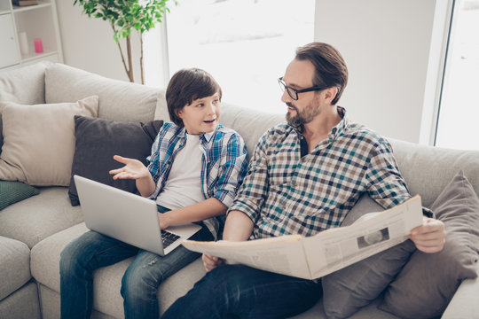 Profile side view portrait of two nice attractive cheerful smart clever guys dad and pre-teen son sitting on sofa typing on laptop reading news talking in light white modern interior house living-room