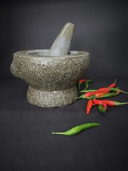 Stone mortar and pestle with some green and red chili peppers are on black background
