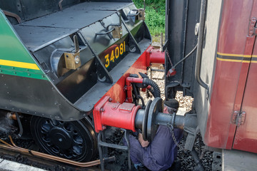 Steam engine driver seen crouching in front of his steam train, de-coupling a passenger car so the train can be shunted to its shed.