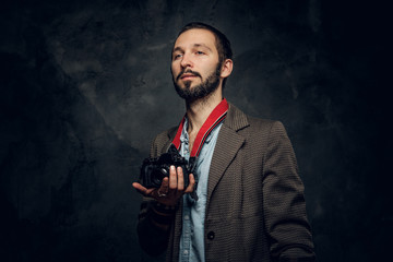 Portrait of bearded young reporter with photo camera at dark photo studio.