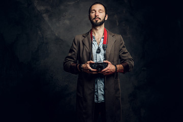 Portrait of bearded young reporter with photo camera at dark photo studio.