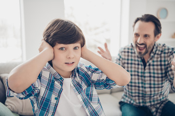 Fototapeta premium Close-up portrait of two guys evil outraged aggressive dad and scared pre-teen son in casual checkered shirt closing ears having fight disagreement in light white modern style interior house