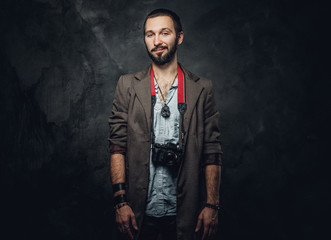 Portrait of smiling bearded reporter with photo camera on the dark background.
