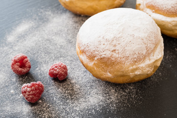 Beignets/german donuts - berliner with raspberries and powdered sugar on the dark background