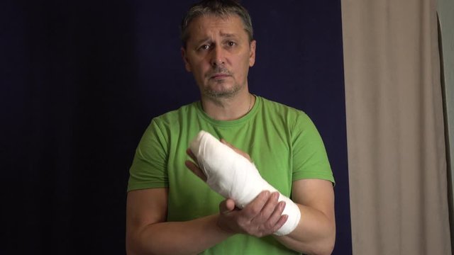 A man scratches his arm in a cast . Man's hand in bandages after surgery.