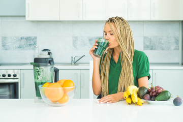 Woman drinking green spirulina in a white kitchen. Vegan meal diet at home. Ideal weight and weight...