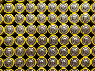 A large number of old yellow AA batteries. Batteries laid out in a square shape.