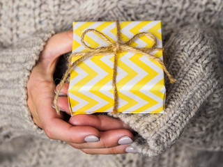 A gift wrapped in yellow paper lies in the hands of women.