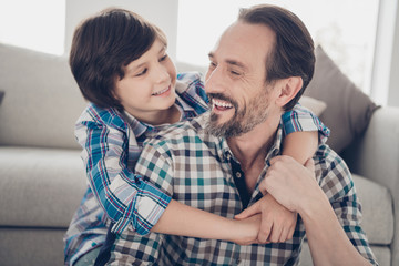 Close-up portrait of two nice attractive tender cheerful cheery glad guys dad daddy and pre-teen son hugging spending day at light white modern style interior house living-room indoors