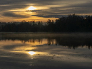 early autumn morning, white mist over water and ground, beautifully colored and blurred tree silhouettes in the background