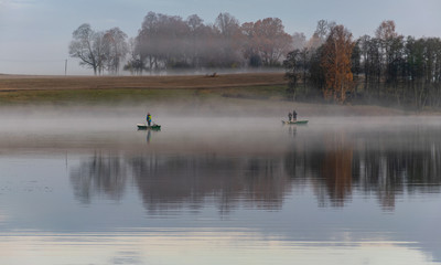 early autumn morning, white mist over water and ground, beautifully colored and blurred tree silhouettes in the background