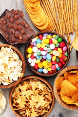 Salty snacks. Pretzels, chips, crackers in wooden bowls and candy and chocolate on table