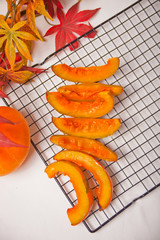 Fresh pumpkin cut in pieces of a oven metal baking rack with herbs and spices with colorful autumn leaves on the background