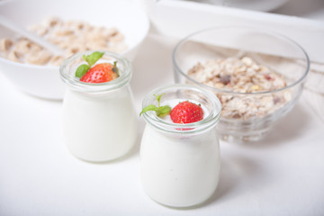 Two portions natural homemade yogurt in a glass jar with fresh strawberry and muesli nearby