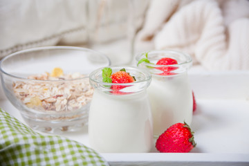 Two portions natural homemade yogurt in a glass jar with fresh strawberry and muesli nearby
