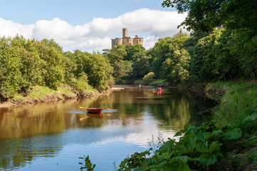 Fototapeta na wymiar Rowing boats on the River Coquet with Warkworth Castle in the background