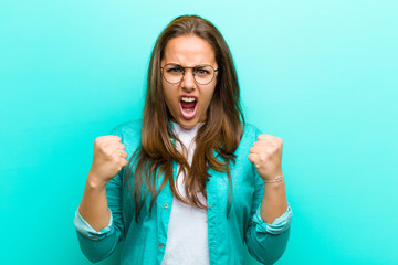 young woman shouting aggressively with annoyed, frustrated, angry look and tight fists, feeling...