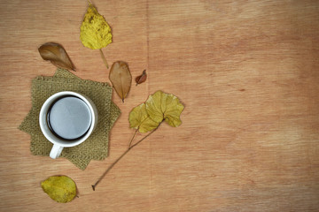 Autumn composition concept. Cup of coffee with autumn leaves on wooden background.