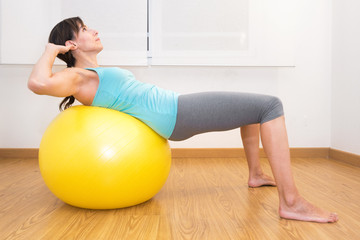 Woman working out with exercise ball in gym. Pilates woman doing exercises in the gym workout room with fitness ball .