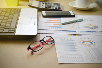 Financial graphs and charts with eyeglasses, calculator, smartphone and coffee on desk. office supplies concept.