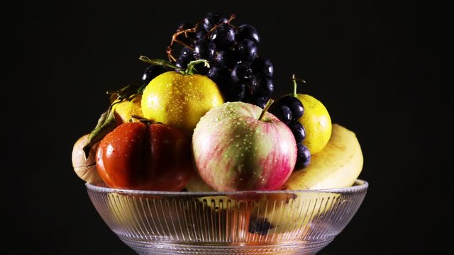 A vase with fresh fruit and water droplets on them rotating on a black background