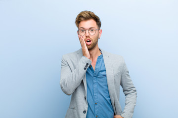 young businessman feeling shocked and astonished holding face to hand in disbelief with mouth wide...