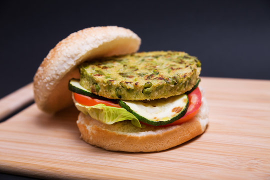 Hamburguesa vegana de guisantes y jud&iacute;as verdes con lechuga, tomate y calabac&iacute;n en una table de madera sobre fondo negro.