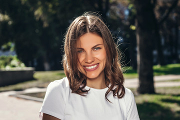 Portrait of a young cute girl in a white T-shirt with a smile in the park. Attractive girl smiling...