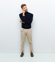 young full body man with a concentrated look, wondering with a doubtful expression, looking up and...
