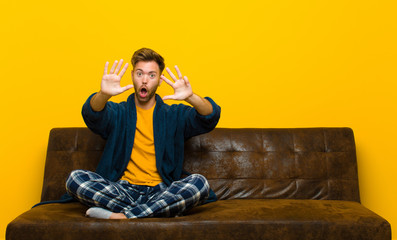 young man wearing pajamas smiling and looking friendly, showing number nine or ninth with hand...