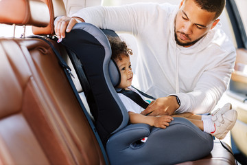 Side view of father fastening his little son safely in a car seat
