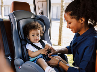 Mother fastening her little son safely in a car seat