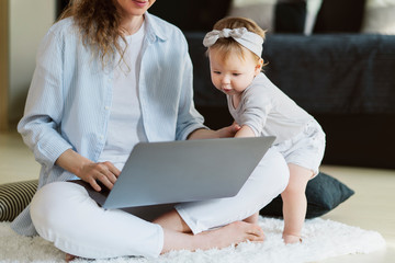 Little girl standing near laptop held by mother, pointing screen. Mother showing educating videos for developing children's skills