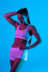 Obraz premium Young sportswoman with perfect body isolated on blue light background