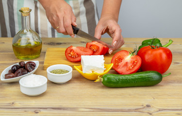 Woman preparing Greek salad. Ingredients for Greek Salad on wooden background. Vegetables on wooden background. Healthy food, Mediterranean diet. Girls cooking Greek Salad. Copy space for text.
