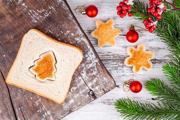 Slice of toast bread with a toasted cut out shaped like a fir tree on a rustic wooden cutting board and snowflake in winter holidays decorations. Concept of Christmas and New Year breakfast food.