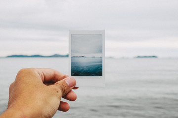 Close up of man's hand holding photograph of sea