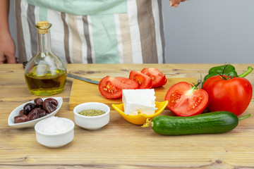 Woman preparing Greek salad. Ingredients for Greek Salad on wooden background. Vegetables on wooden background. Healthy food, Mediterranean diet. Girls cooking Greek Salad. Copy space for text.