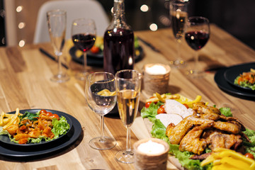 Festive table setting. Food and drinks, plates and glasses. Evening lights and candles. New Year's Eve.