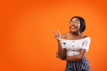 Happy African American Girl Pointing Finger Aside Standing, Orange Background