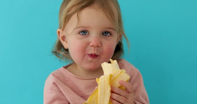 Funny Portrait of a young girl eating banana on a blue studio background