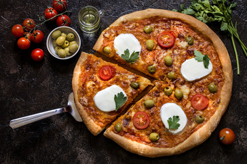 pizza with mozzarella and tomato sauce, herbs and olives on a dark background