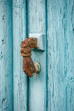 rusty hand shaped door knocker on wooden door with weathered blue paint in traditional village Kalarites, Greece