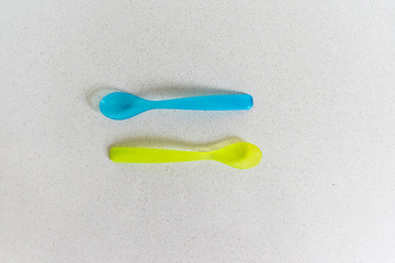 Blue and geen baby spoon. Plastic isolated on grey stone background. 