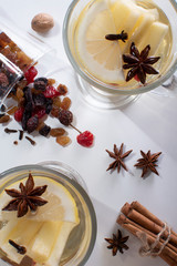Top view of two glasses with white mulled wine with a sliced apple, a slice of lemon and anise, a jar of dried fruit sprinkled on a wooden table.