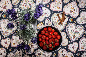 Delicious ripe strawberries on black plate on table with a colorful tablecloth. Flat lay