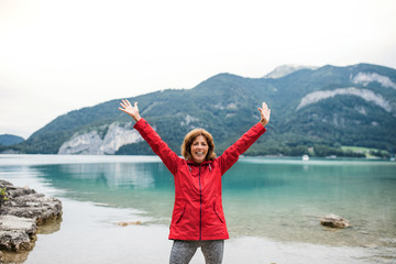 A senior woman hiker standing by lake in nature, stretching arms.